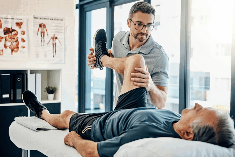 Physiotherapist performing a leg mobility assessment on an older male patient lying on a treatment table in a bright, modern clinic.