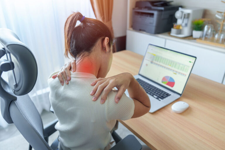 Woman sitting at a desk with a laptop, holding her neck and shoulder in pain, with a red highlight indicating muscle strain or tension from poor posture or prolonged computer use.