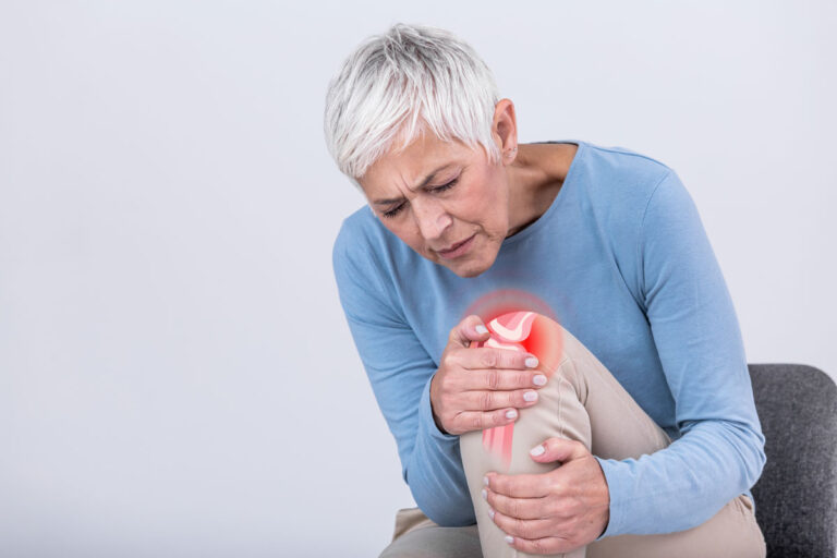 Older woman sitting and holding her knee in visible discomfort, with a red glow and joint graphic overlay highlighting knee pain or joint inflammation.