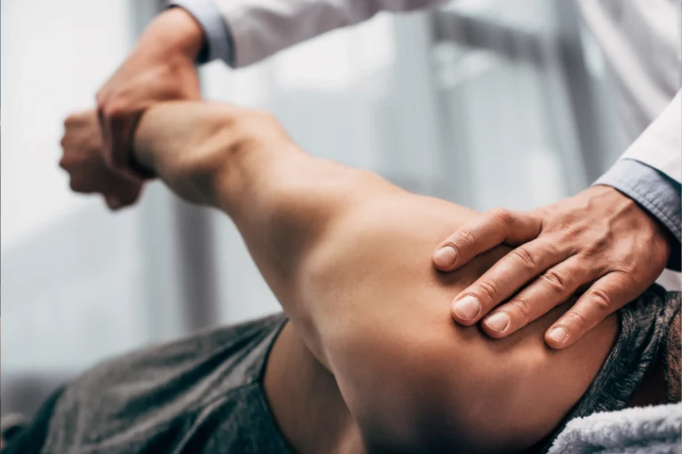 Close-up of a physiotherapist performing manual therapy on a patient’s shoulder, supporting and mobilizing the joint in a clinical setting.