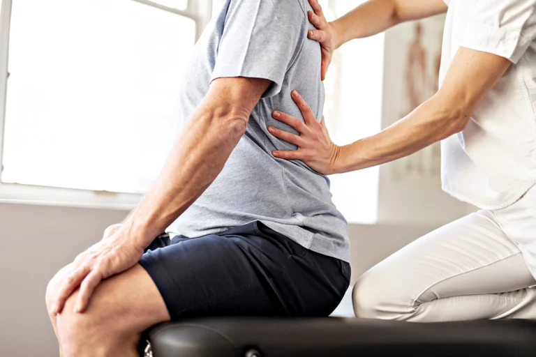 Physiotherapist assessing the posture and spinal alignment of a seated patient by gently placing hands on the upper and lower back in a clinical setting.
