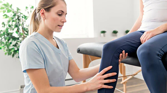 Physiotherapist assessing a patient's knee in a bright, modern clinic, focusing on joint alignment and mobility during a seated evaluation.
